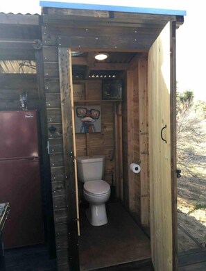 A small wooden structure with a toilet, a sink, and a refrigerator.