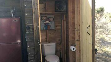 A small wooden structure with a toilet, a sink, and a refrigerator.