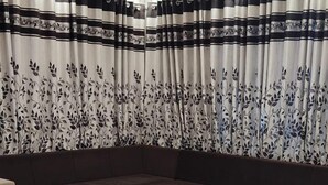 Een moderne woonkamer met een hoekbank, een glazen salontafel, gordijnen met een patroon en een plafondventilator.