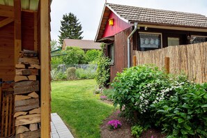 Ein Holzhaus mit einer Steinstufenanlage, einem eingezäunten Hof und einem Garten mit verschiedenen Pflanzen.