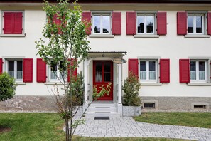 A building with red shutters, a white facade, and a number '29' sign.