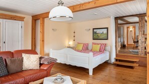 A room with a wooden ceiling, a white bed with red and yellow checkered bedding, a brown leather sofa, and a wooden coffee table. - Apartment 'Belchenwind Typ B, 65sqm, Terrace' with Mountain View, Private Terrace & Wi-Fi (Münstertal)