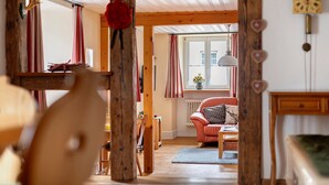 A cozy room with wooden beams, a red chair, a wooden table, and a window with curtains. - Apartment 'Belchenwind Typ B, 65sqm, Terrace' with Mountain View, Private Terrace & Wi-Fi (Münstertal)