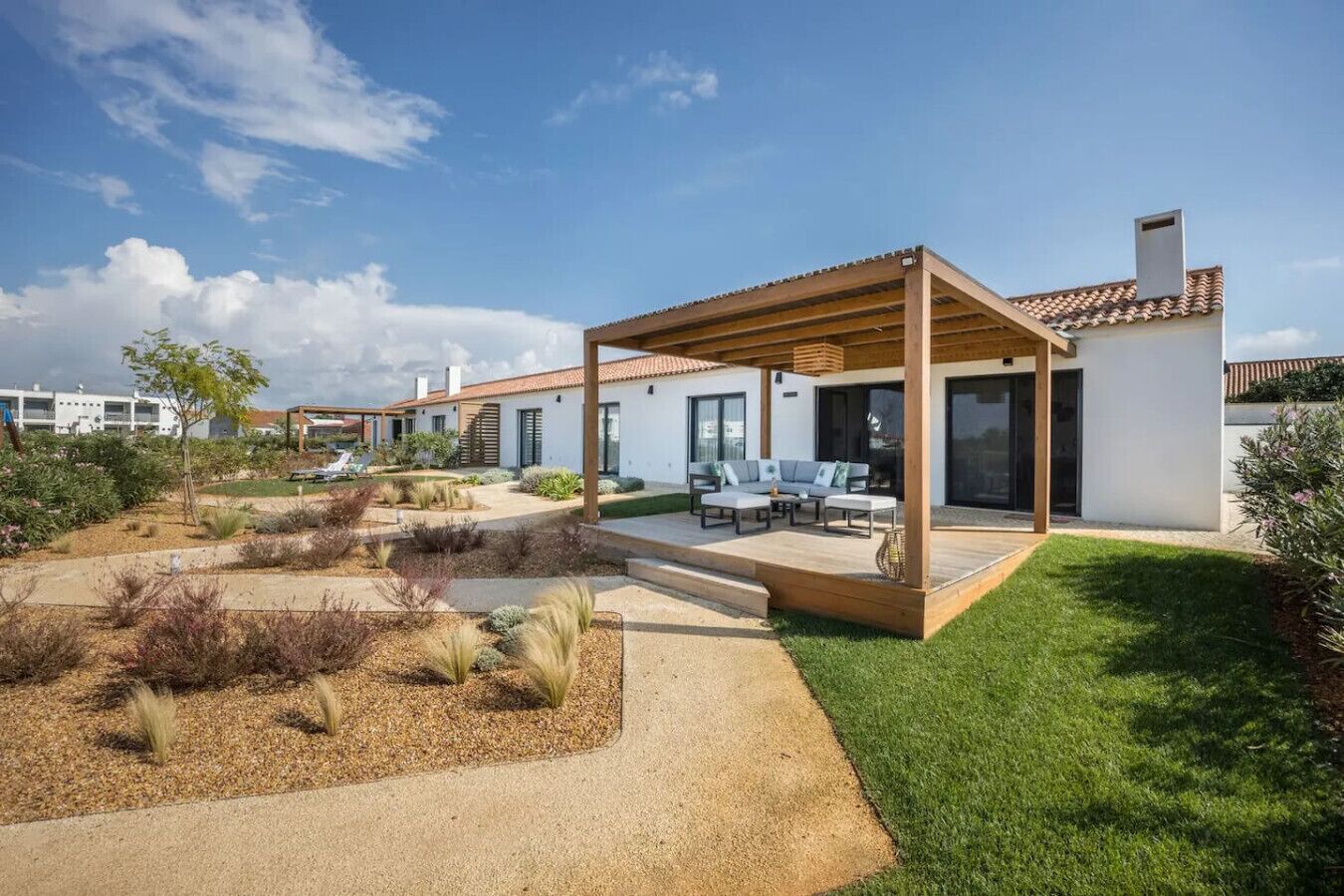 Ein modernes Haus mit überdachter Terrasse, einem gepflegten Garten und blauem Himmel.