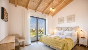 Ein Schlafzimmer mit einem Bett, Nachttischen, einem Schreibtisch und einem Stuhl. Ein großes Fenster bietet einen Ausblick ins Freie.