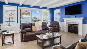 A living room with a fireplace, leather sofas, a coffee table, and large windows with a view of the lake.
