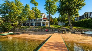 A waterfront property with a wooden dock, a stone wall, and a large house with a balcony.