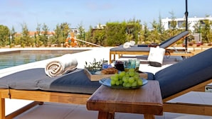 A poolside lounge area with a table set with a plate of grapes, a bottle, and a glass.
