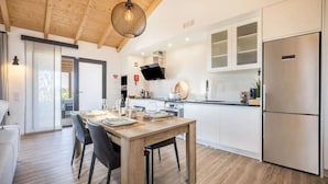 A modern kitchen with white cabinets, a stainless steel refrigerator, and a dining area with a wooden table and chairs.