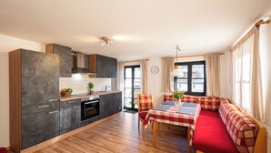 Eine moderne Küche mit Essbereich, ausgestattet mit einer rot-weißen karierten Tischdecke, einer hölzernen Bank und Blick ins Freie durch große Fenster.