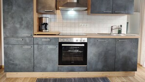 Eine moderne Küche mit grauen Schränken, einem eingebauten Backofen, einer Kaffeemaschine und einer Edelstahl-Dunstabzugshaube.