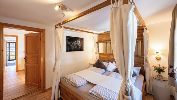 Ein Bett mit Baldachin, ein hölzerner Kopfteil, ein Nachttisch mit Lampe und ein gerahmtes Bild an der Wand.