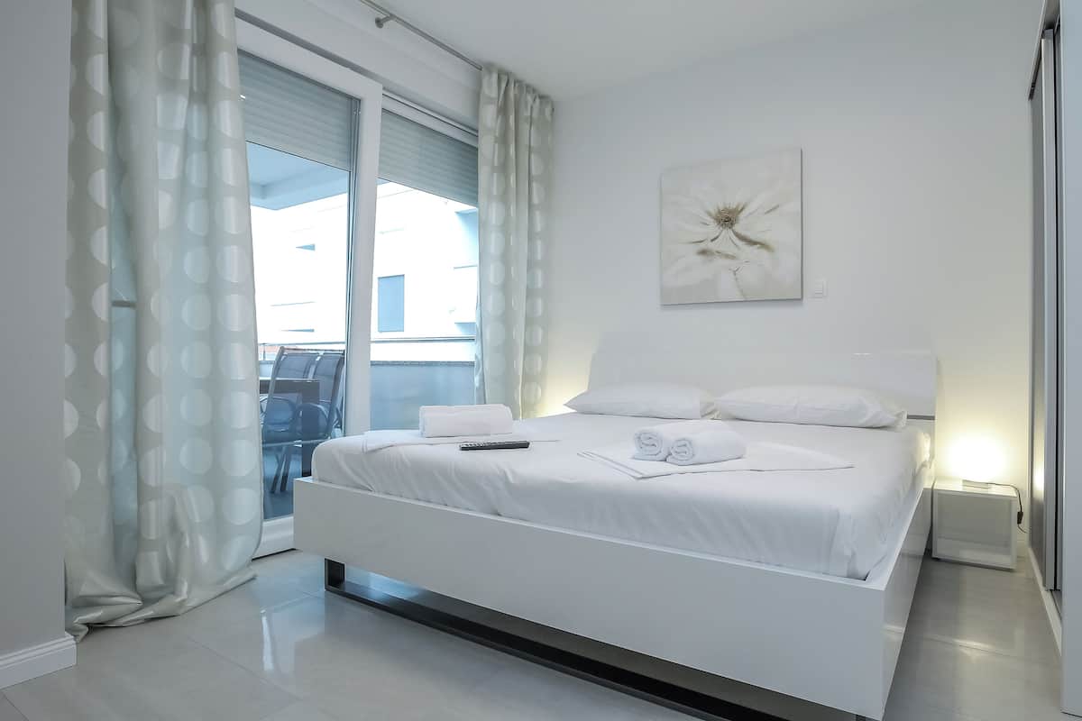 Habitación de hotel moderna con una cama grande, un cuadro en la pared y vistas al exterior a través de la ventana.