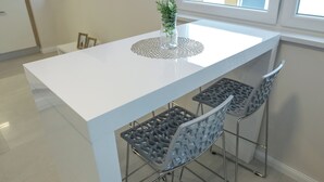 Ett modernt kök med en vit bänkskiva, två barstolar och en vas med gröna växter.