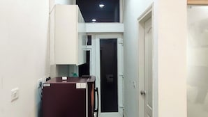 A narrow hallway with a refrigerator, a door, and a ceiling light. - Let'stay- NX-One Noida (Greater Noida)