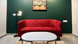 A room with a red sofa, a round table, a green wall, and a framed picture of mountains. - Let'stay- NX-One Noida (Greater Noida)