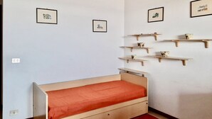 Pieni huone, jossa on yksi sänky. Sängyssä on puinen sängynrunko ja punainen patja. Seinällä on kolme kehystettyä kuvaa, ja seinällä on myös useita puisia hyllyjä, joilla on koriste-esineitä.