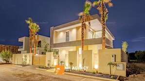 A modern two-story residential building with a well-lit entrance, palm trees, and a gated driveway. - Villa Akenza (Marrakech)