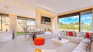 A modern living room with a sofa, coffee table, and TV. There is a dining area with a table and chairs. - Villa Akenza (Marrakech)