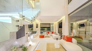 A modern living room with a white sofa, orange ottoman, and a glass wall. - Villa Akenza (Marrakech)