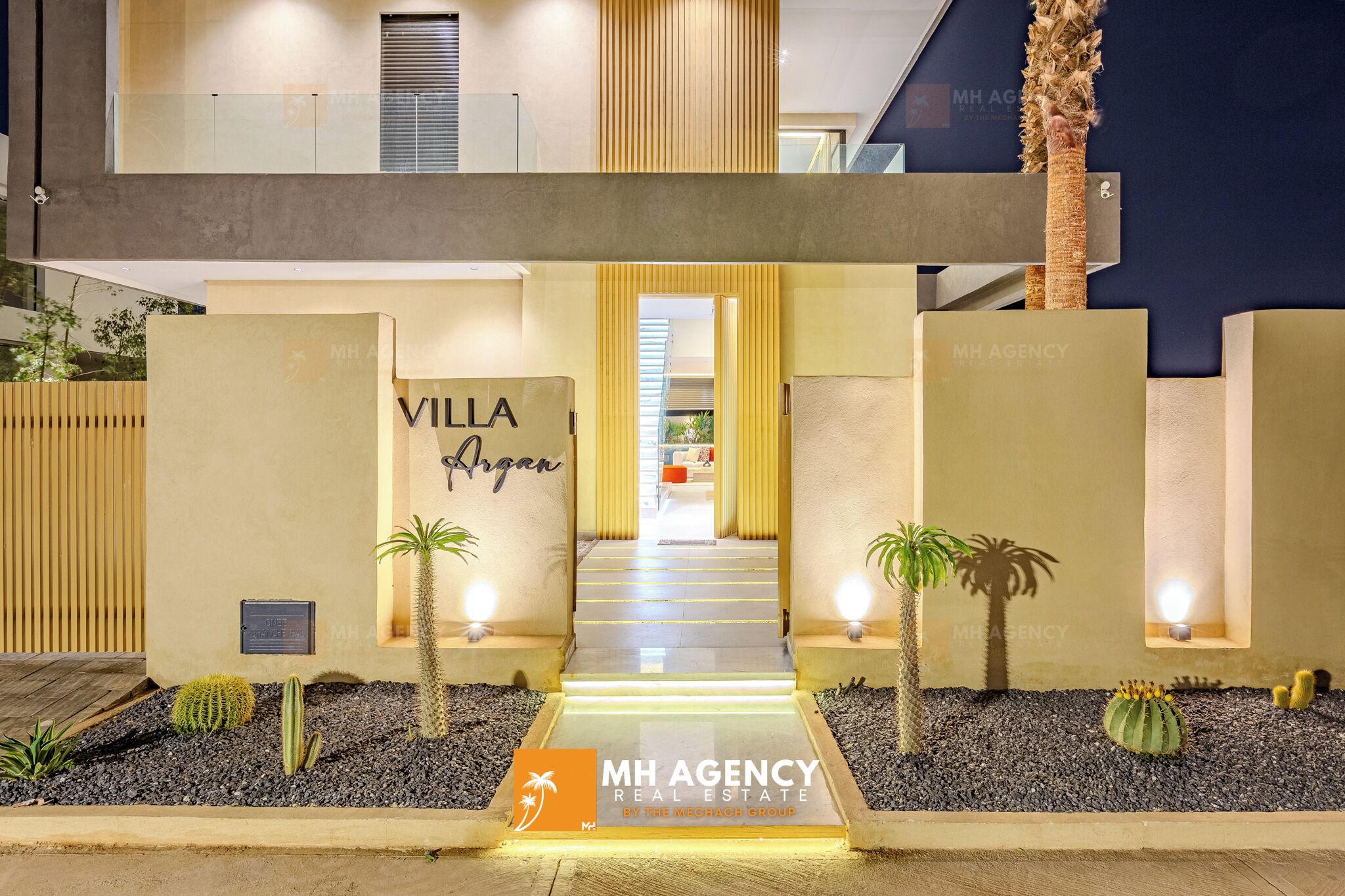 A modern villa entrance with a well-lit pathway, a sign reading "Villa Aragon," and a logo for MH Agency Real Estate.