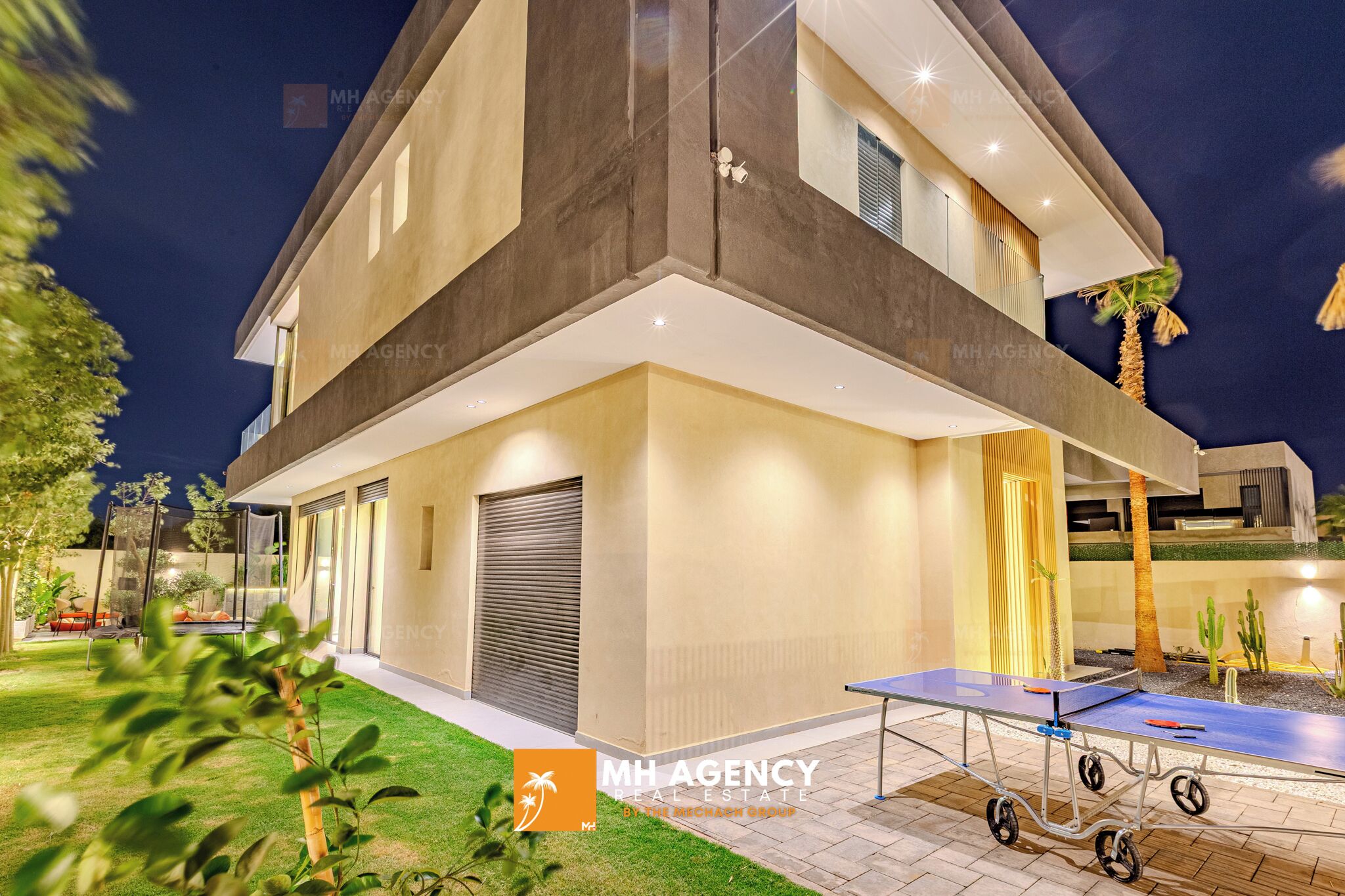 A modern two-story house with a well-lit patio area, a ping pong table, and a covered seating area.