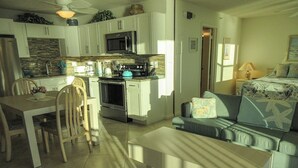 A modern kitchen with white cabinets, a microwave, and a stove. There is a dining table with chairs and a sofa in the living area. - Estero Beach & Tennis Club 1105A! Gorgeous Direct Gulf View! (Fort Myers Beach)