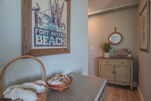 Ein Zimmer mit einem gerahmten Poster eines Schiffes, einem Muschelnkorb und einer kleinen Topfpflanze auf einer Holzdresser.