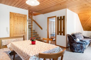Ein Zimmer mit einer Holztreppe, einem Esstisch mit blumigem Tischläufer und einem gemusterten Sofa.