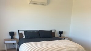 Une chambre à coucher avec un lit, deux tables de chevet avec des lampes, un climatiseur fixé au mur et un plancher en bois.