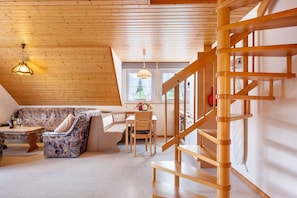 A wooden interior with a staircase, a sofa, a table, and a hanging light fixture.