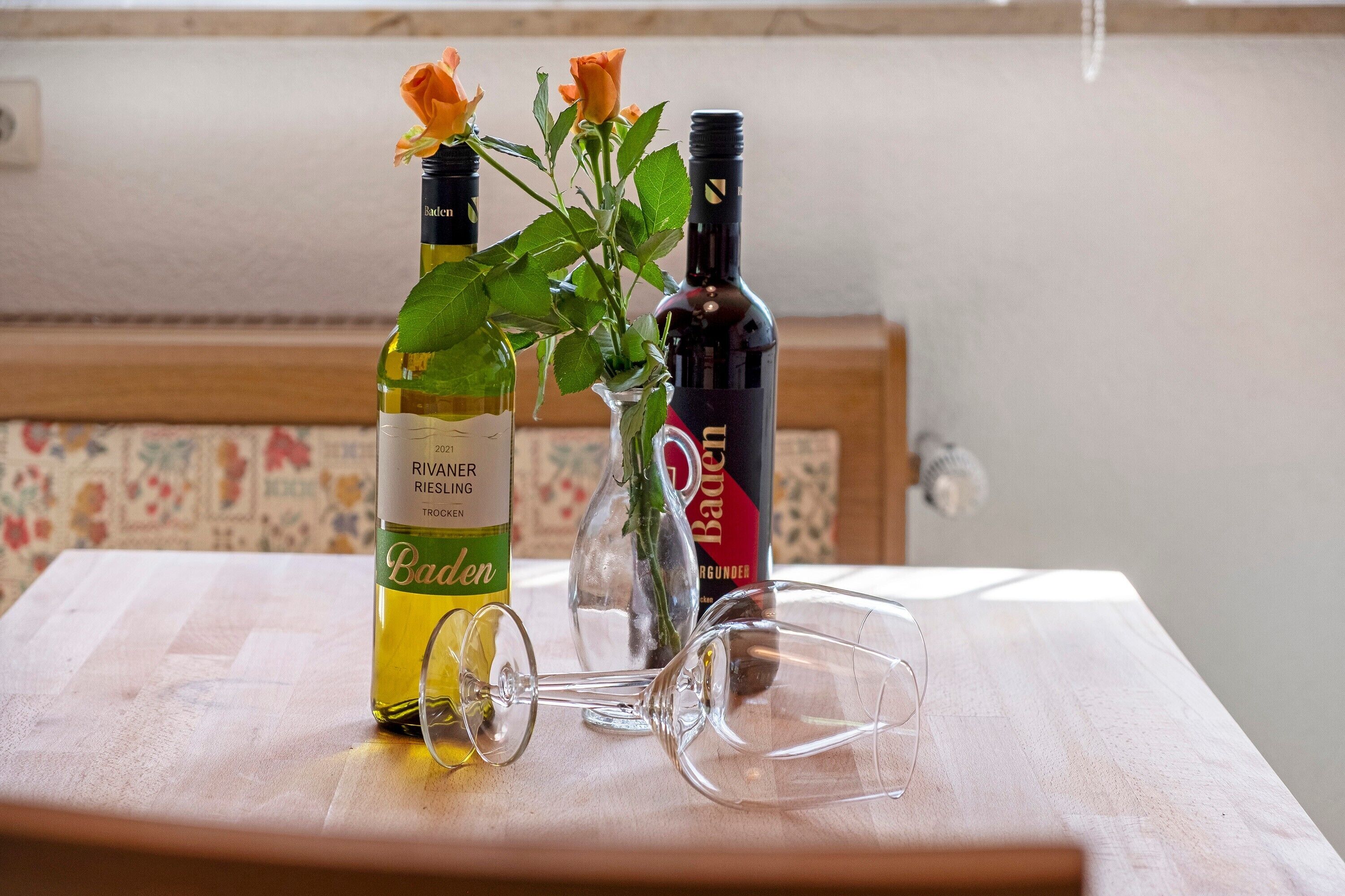 A table with two wine bottles, a glass, and a vase with flowers.