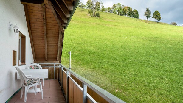 A balcony with a table and chairs, overlooking a grassy hill. - Holiday Apartment with Mountain View 1 with Balcony and Wi-Fi (Wieden)
