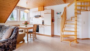 A loft-style room with a wooden ceiling, a dining area with a table and chairs, a kitchen with white cabinets, and a wooden staircase. - Holiday Apartment with Mountain View 1 with Balcony and Wi-Fi (Wieden)