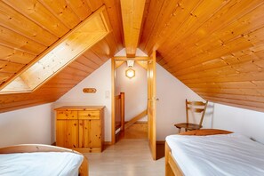 Une chambre avec des poutres en bois au plafond, une lucarne, un lit, une chaise et une commode en bois.