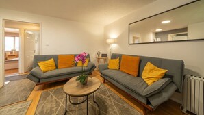 Una sala de estar con dos sofás grises, cojines amarillos, una mesa redonda de madera y una orquídea en maceta.