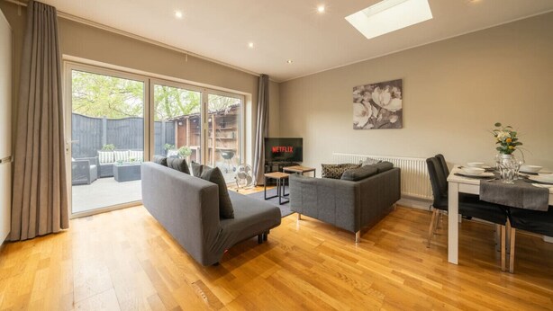 Een woonkamer met een bank, een televisie, een eettafel en een grote schuifdeur die leidt naar een buitenruimte.