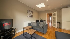 Een moderne woonkamer met een flatscreen televisie, een bank, een salontafel en een eethoek op de achtergrond.