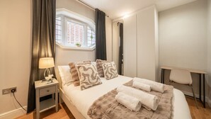 Een slaapkamer met een bed, een bureau, een raam en een nachtkastje.
