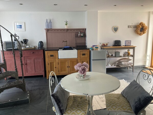 A modern kitchen with a central island, wooden cabinets, and a dining area with a round table and cushioned chairs. - Stunning riverside & waterfall apartment barn, nestled in nature Brecon Beacons (Llangynidr)