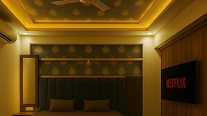 Een slaapkamer met een bed, een plafondventilator, een aan de muur bevestigde tv waarop 'NETFLIX' staat, en een nachtkastje met een lamp.