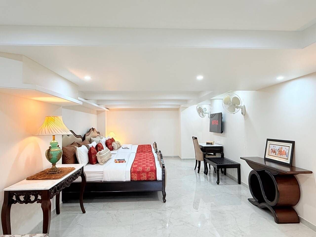 A hotel room with a bed, bedside table, lamp, TV, desk, chair, and a framed picture on the wall.