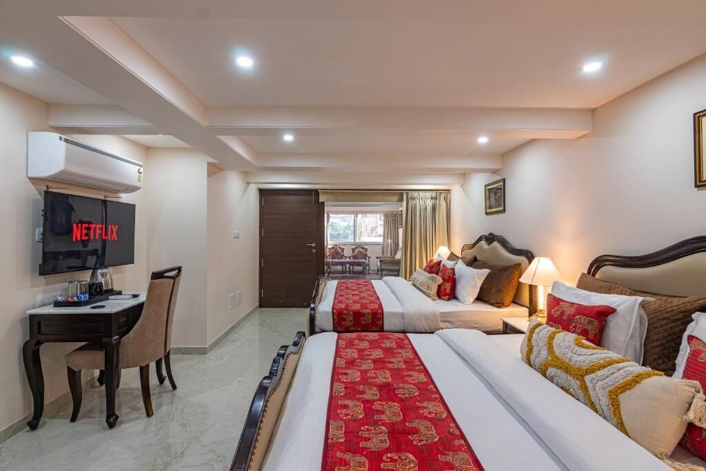 A hotel room with a bed, a desk, a chair, a TV, and a door leading to a balcony.