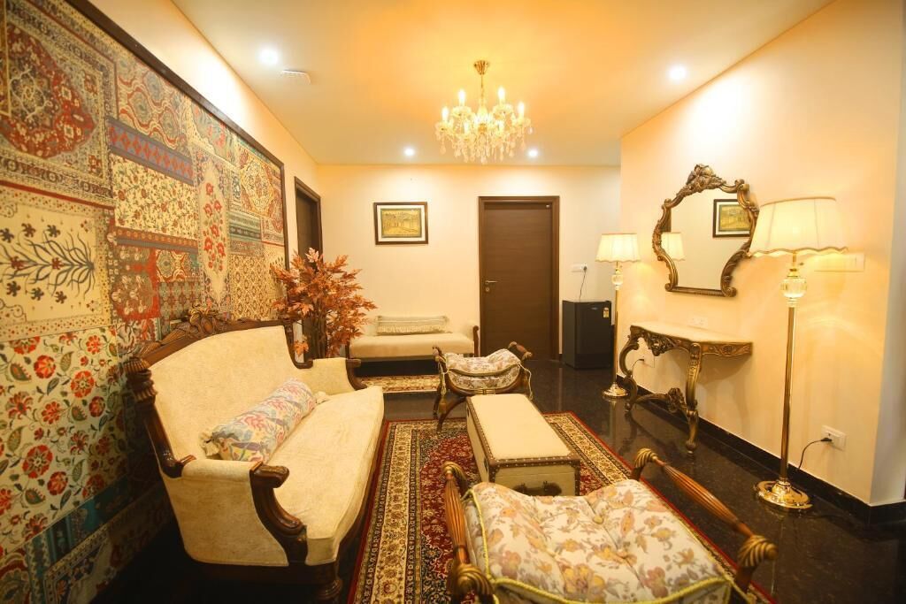 A traditional room with a sofa, armchair, and ottoman, a chandelier, a mirror, and a patterned wall.