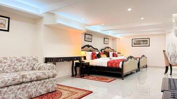 A hotel room with a bed, a sofa, a desk, and a fan.