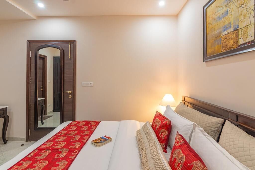 A hotel room with a bed, a nightstand, a lamp, a painting on the wall, and a door leading to another room.