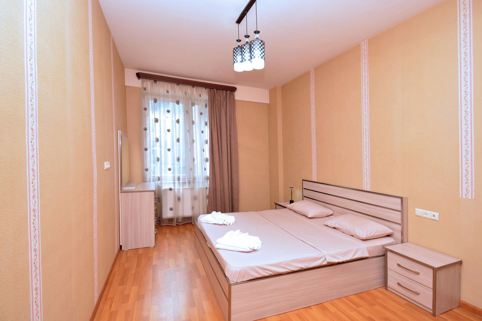 A bedroom with a wooden bed, a bedside table, a nightstand, and a ceiling light fixture.