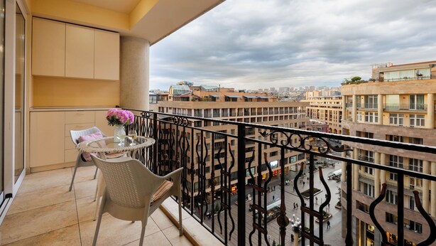 A balcony with a table and chairs, overlooking a cityscape with multiple buildings.