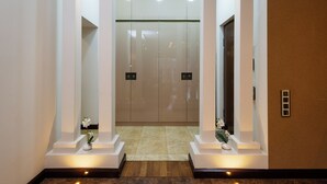 A modern elevator with glass doors, flanked by white pillars and small vases with flowers.