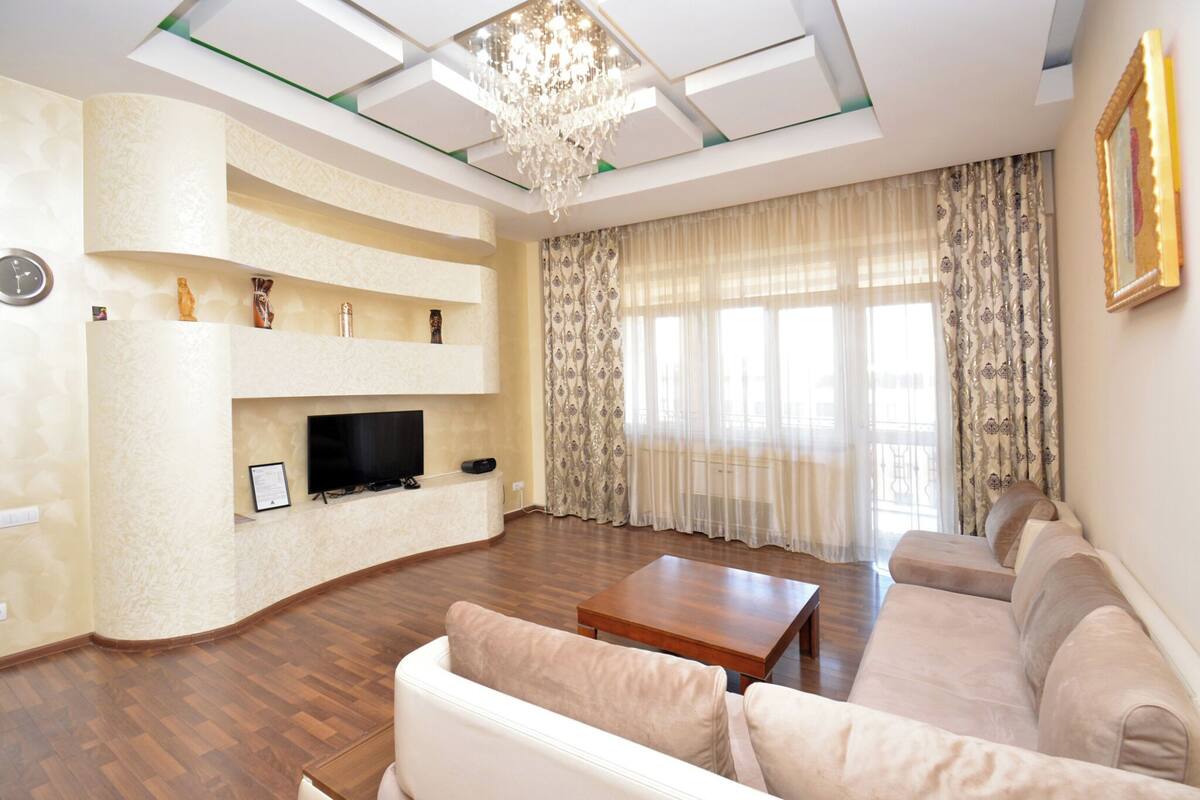 Ein modernes Wohnzimmer mit Flachbildfernseher, Couchtisch aus Holz und beiger Couch.